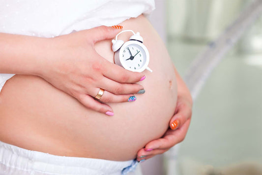 Pregnant woman holding a clock to her stomach